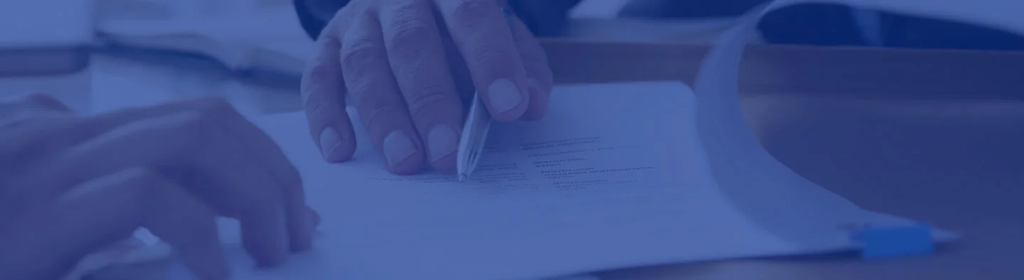 A person's hand signing a document on a desk with a pen.
